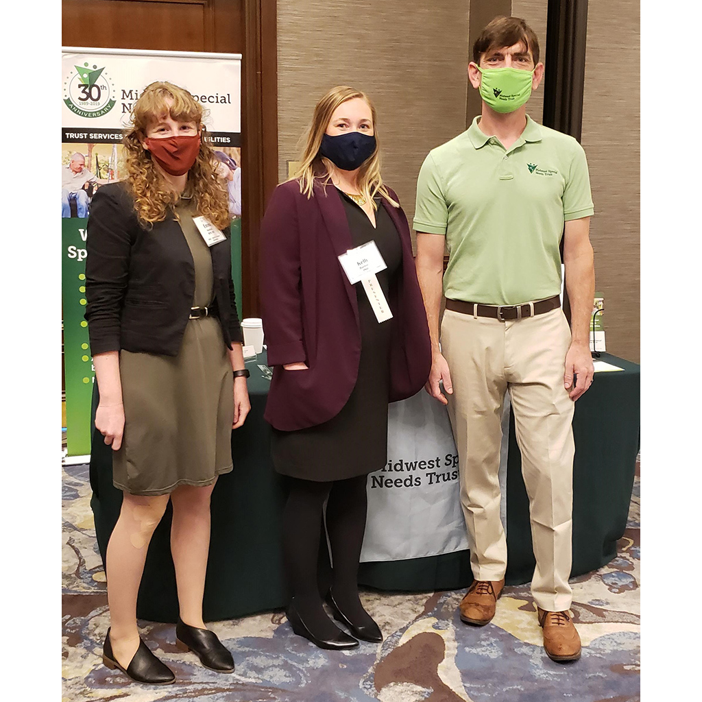 Three professionals standing in front of an exhibit booth for Midwest Special Needs Trust.